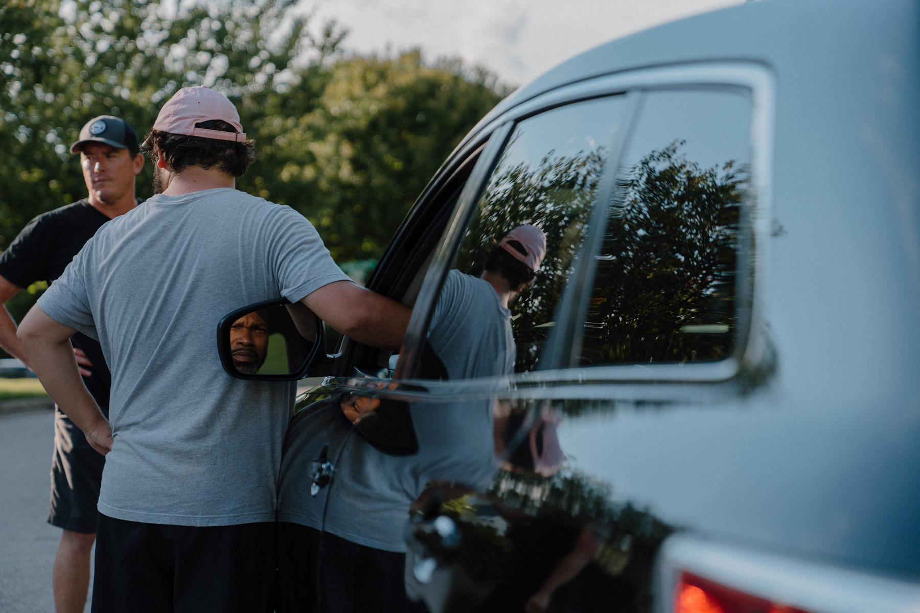 Shot of film crew outside of a car and a driver in a car 