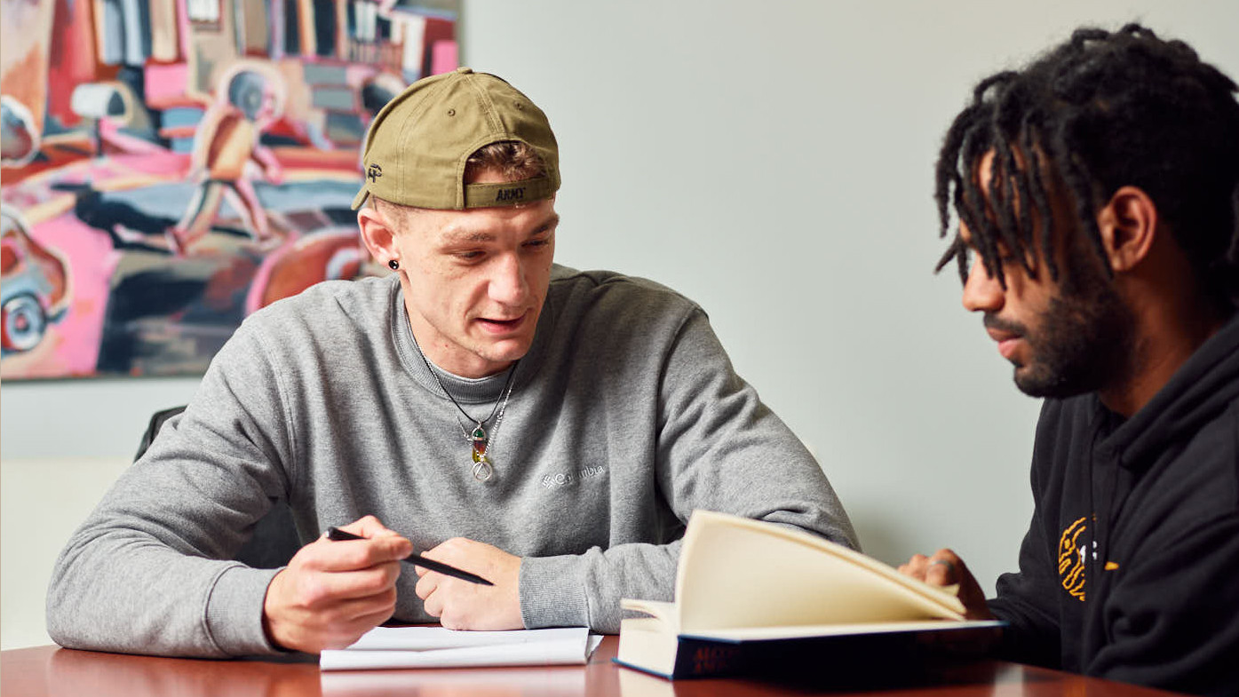 Two people sharing thoughts with a book and notepad between them. 